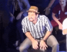 a man wearing a hat and striped shirt is sitting on a chair