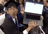 a man in a graduation cap and gown is holding a laptop in his hand .