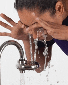a woman is washing her face in a faucet