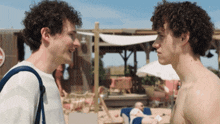 two men with curly hair are looking at each other on a beach with a sign that says do not enter