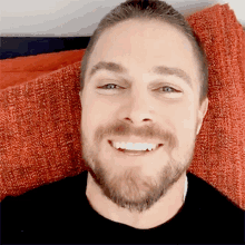 a man with a beard is smiling while laying on an orange blanket