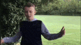 a young boy in a blue vest is standing in a grassy field .