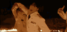 a man in a white military uniform is dancing in front of a fire .