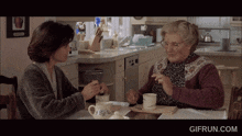 two women sit at a table with a gifrun.com watermark on the bottom right