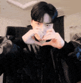 a man in a leather jacket makes a heart shape with his hands