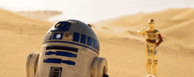 a r2d2 robot is standing next to a c3p0 robot in the desert