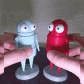a blue robot and a red robot are being touched by someone 's fingers