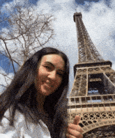 a woman stands in front of the eiffel tower and giving a thumbs up
