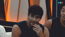 a man in a black tank top is smiling while another man looks on
