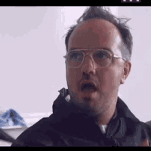 a man wearing glasses and a jacket is making a funny face .