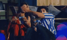 a man and a woman are sitting on a couch covering their faces with their hands .
