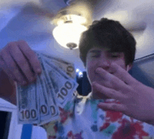 a young man is holding a bunch of money in his hands and covering his mouth .