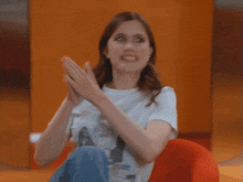 a woman in a white t-shirt is sitting on a red cushion with a caption that says define it