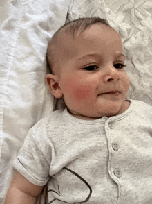 a baby with red cheeks is laying on a white blanket