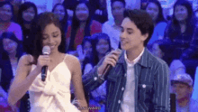 a man and a woman are sitting next to each other in front of a crowd while a man holds a microphone .