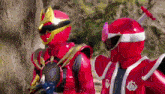 a couple of red rangers are standing next to each other in a forest .