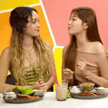 two women sitting at a table with plates of food and drinks