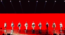 a group of men are standing on a stage in front of a red background