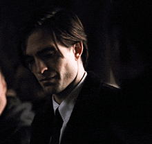 a man in a suit and tie looks at the camera in a dark room