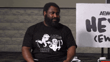 a man sitting in front of a sign that says " he 's crew "