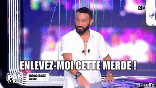 a man with a beard is standing in front of a screen that says enlevez-moi cette merde