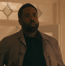 a man in a trench coat is standing in front of a window with saint-pierre written on it