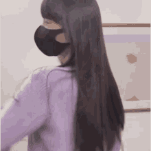 a woman wearing a purple sweater and a black face mask is standing in front of a picture .