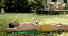 a shirtless man in yellow shorts is laying in the grass reading a book .