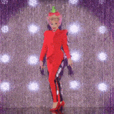 a drag queen in a red suit with a green frog on her hat