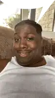 a man in a white tank top sits on a couch and smiles