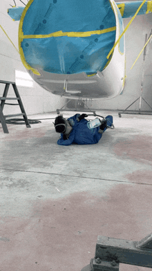 a person is laying on the floor in front of a plane that is being painted
