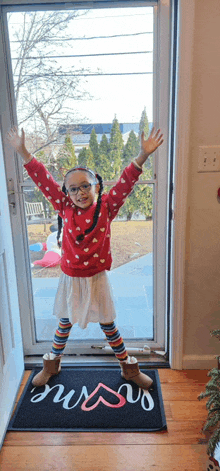 a little girl standing in front of a door wearing a red sweater with hearts on it