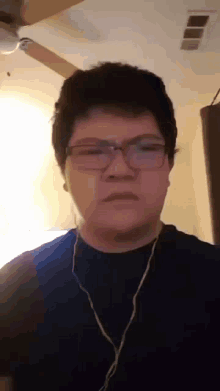 a young man wearing glasses and headphones looks at the camera with a ceiling fan in the background