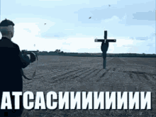 a man is standing in a field with a cross in the background and the words atcasiiiiiiiii in white letters .
