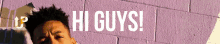 a man is standing in front of a purple brick wall with the words hi guys written on it