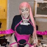 a woman with pink hair and pink gloves is standing in a room with her arms outstretched and smiling .