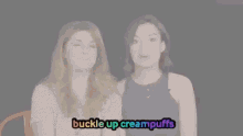 two women are laughing and looking at each other with the words `` buckle up creampuffs '' written on the screen .