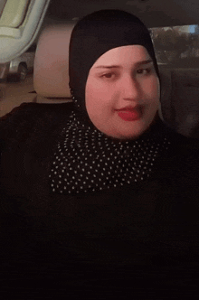 a woman wearing a polka dot scarf and a black head scarf is sitting in a car