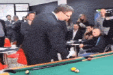 a man in a suit is playing pool with a group of people .