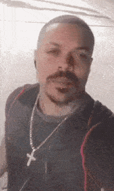 a man with a mustache and a cross necklace is taking a selfie with his phone .