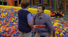 a man and a boy are playing in a ball pit filled with colorful balls .