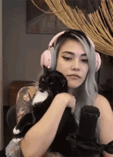 a woman wearing pink headphones is holding a black and white cat in her arms .
