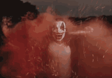 a man in a clown mask is holding a bat in a field of red smoke
