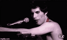 a man without a shirt is singing into a microphone while playing a piano .