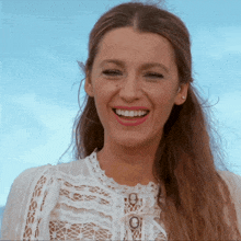 a woman wearing a white lace top is smiling with a blue sky in the background