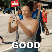 a woman is taking a picture with her phone and the word good is visible
