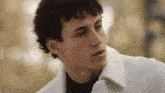 a young man with curly hair wearing a white jacket