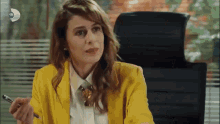 a woman in a yellow jacket sits in an office chair holding a pen