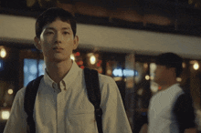 a man wearing a white shirt and a black backpack looks at the camera