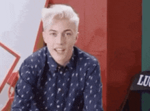 a young man in a blue shirt is sitting in front of a red wall .
